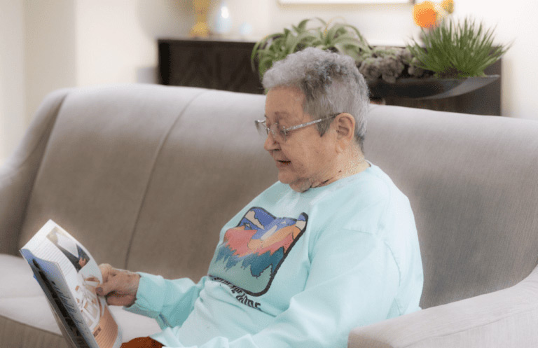 An older woman sits on a couch in Yukon, OK, engrossed in reading a magazine.